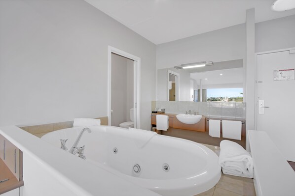 A modern bathroom with a large bathtub, a separate shower area, and a vanity with a sink and mirror. - Bellevue on the Lakes (Lakes Entrance)