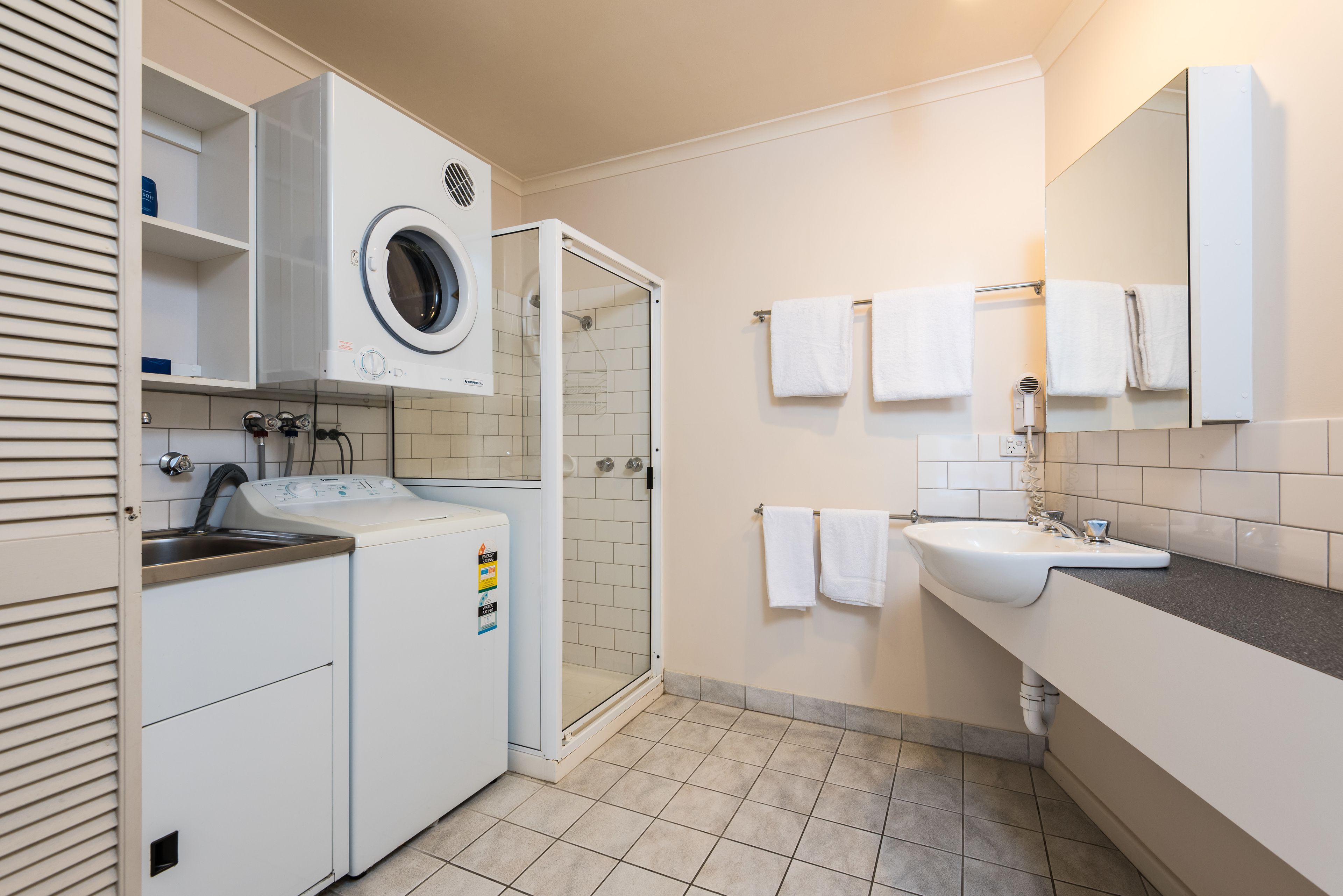 A modern bathroom with a built-in washer and dryer, a shower, and a sink with a mirror.