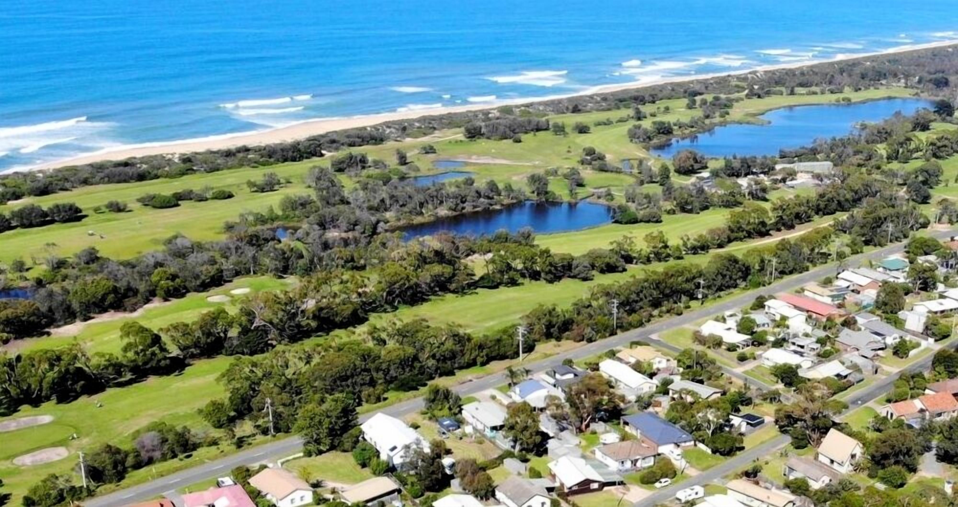 An aerial view of a coastal residential area with houses, a beach, and a lake.