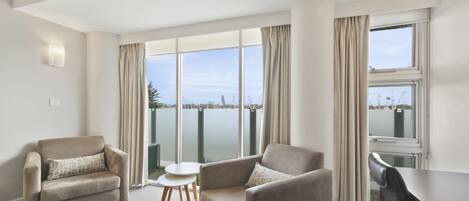 A modern hotel room with two sofas, a small round table, and a large window offering a view of the city.