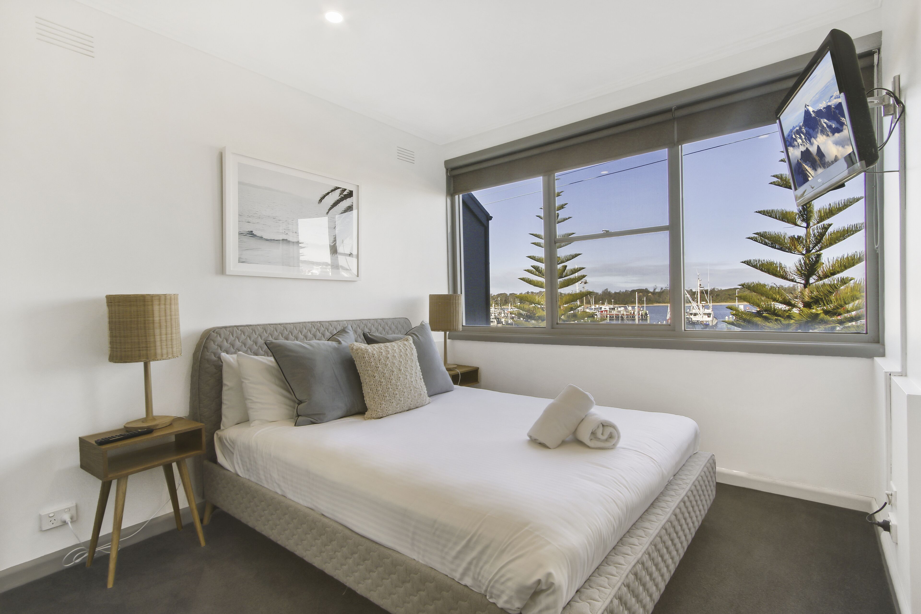 A neatly made bed with a view of a cityscape through a large window.