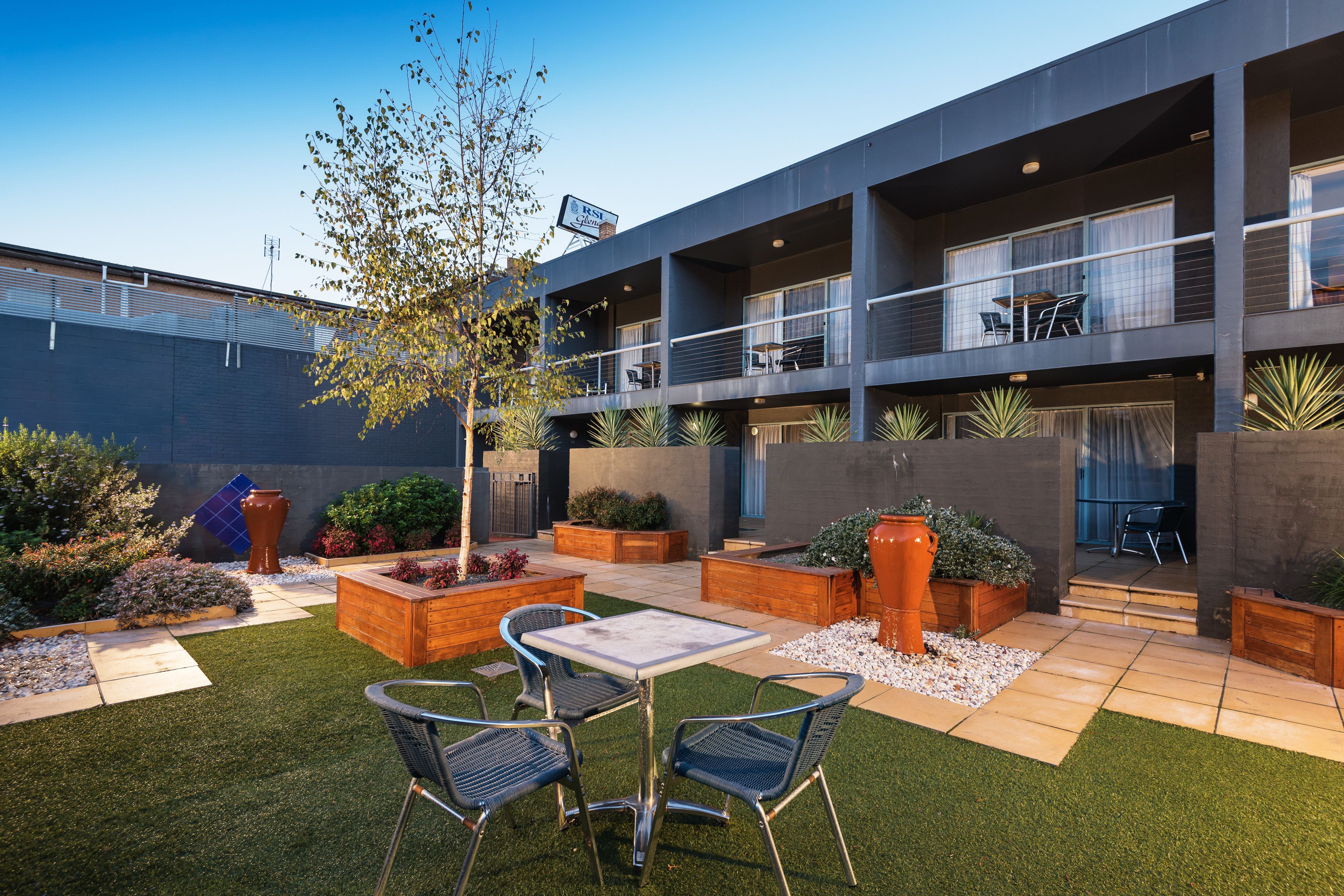 A modern building with a courtyard featuring artificial grass, outdoor seating, and planters.