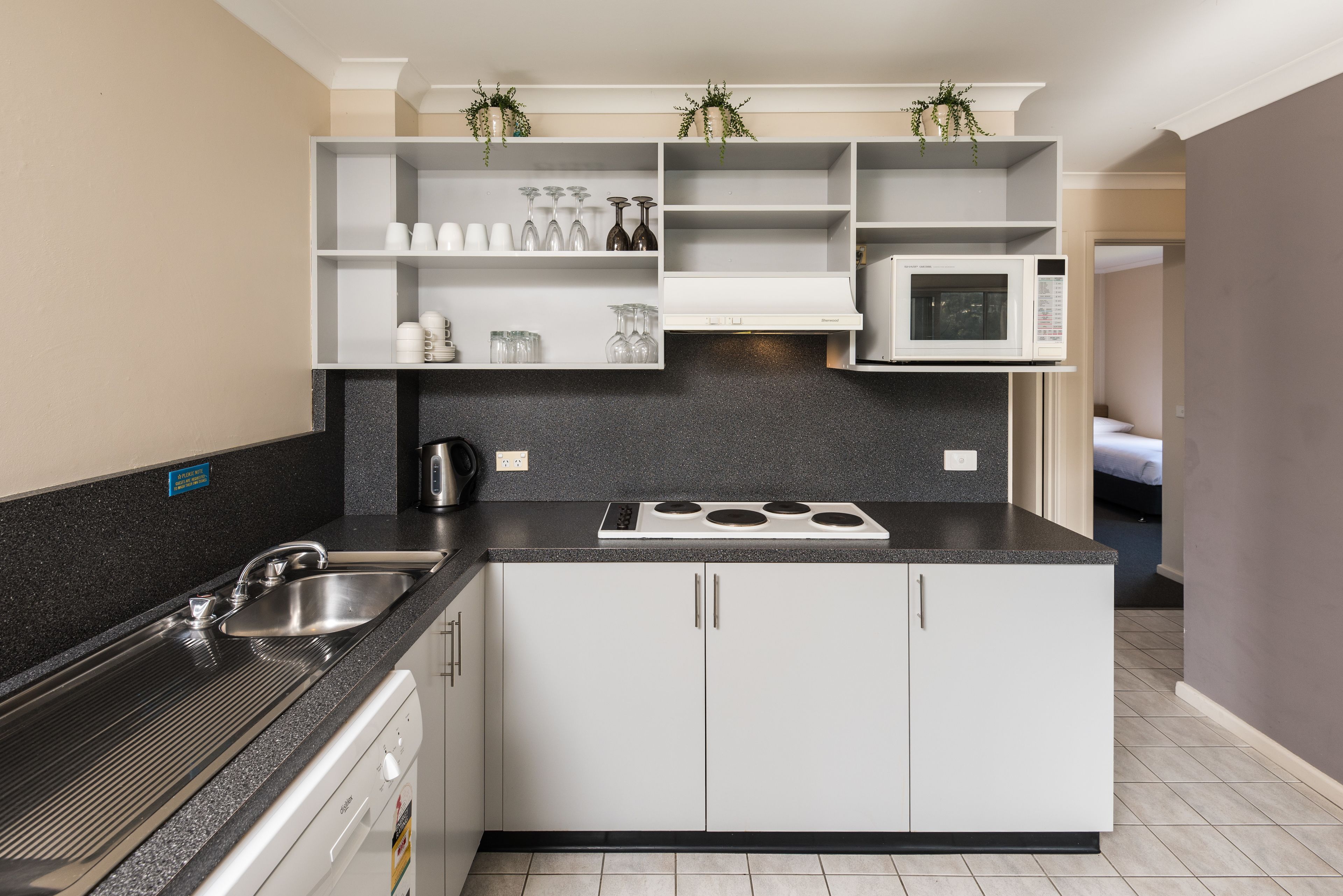 A modern kitchen with white cabinets, a black countertop, a built-in microwave, and a stainless steel sink.