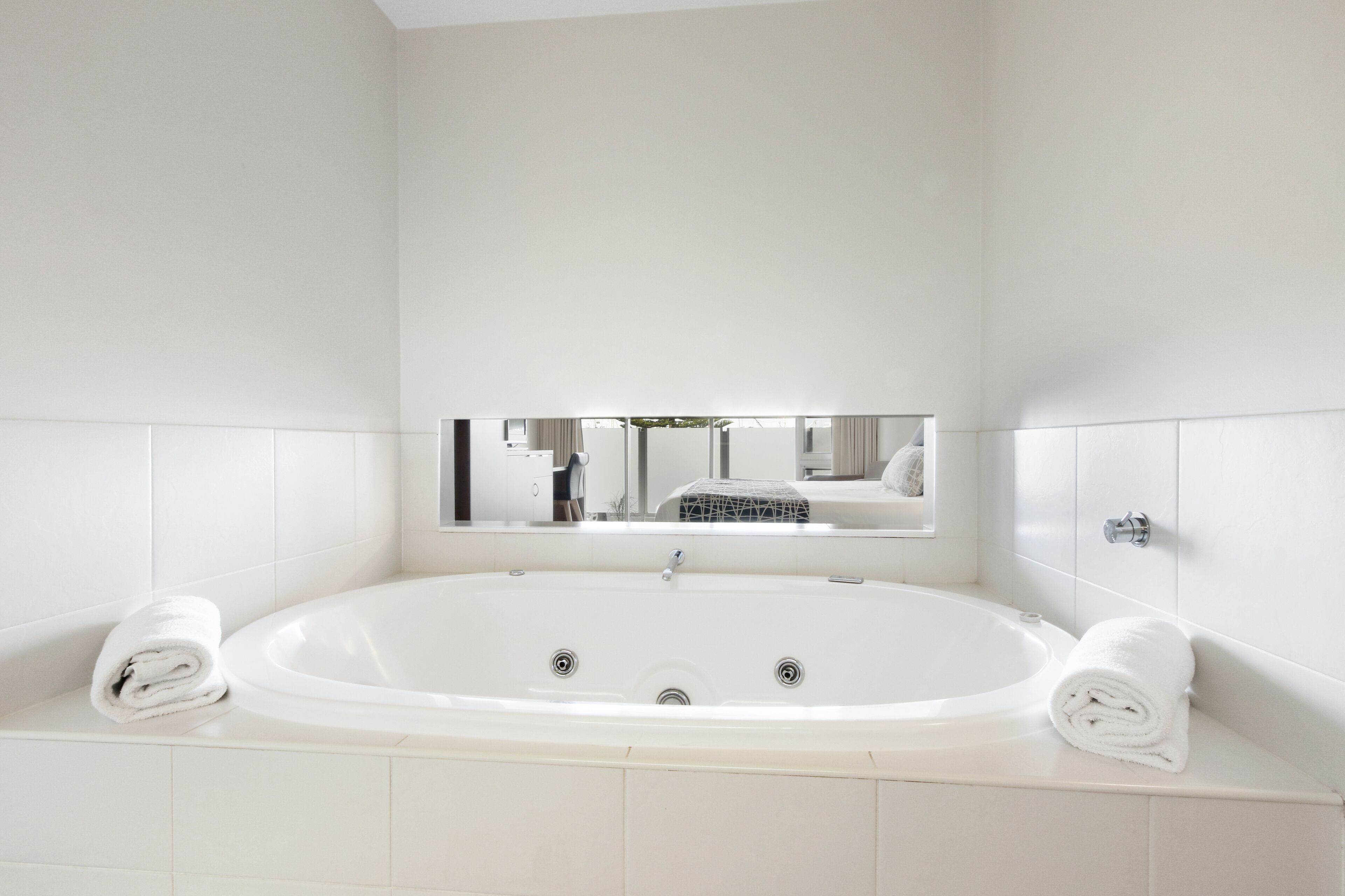 A modern bathroom with a large bathtub, two towels, and a mirror above the tub.