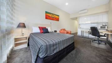 Habitación de hotel con cama, escritorio, silla, lámpara y un cuadro en la pared.