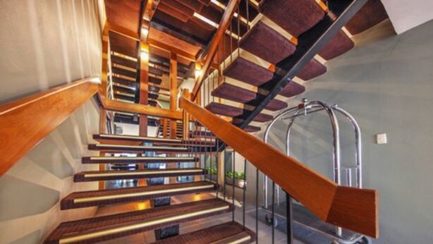 Una escalera moderna con escalones de madera y barandillas de metal, que sube a un piso superior.