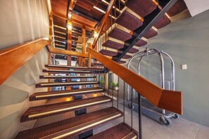 Una escalera moderna con escalones de madera y barandillas de metal, que sube a un piso superior.