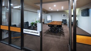 Una sala de conferencias con una mesa grande, sillas, una pizarra y un cartel que indica un salón para huéspedes.