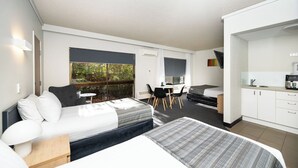 Una habitación de hotel moderna con cama, escritorio, silla, mesita y kitchenette.