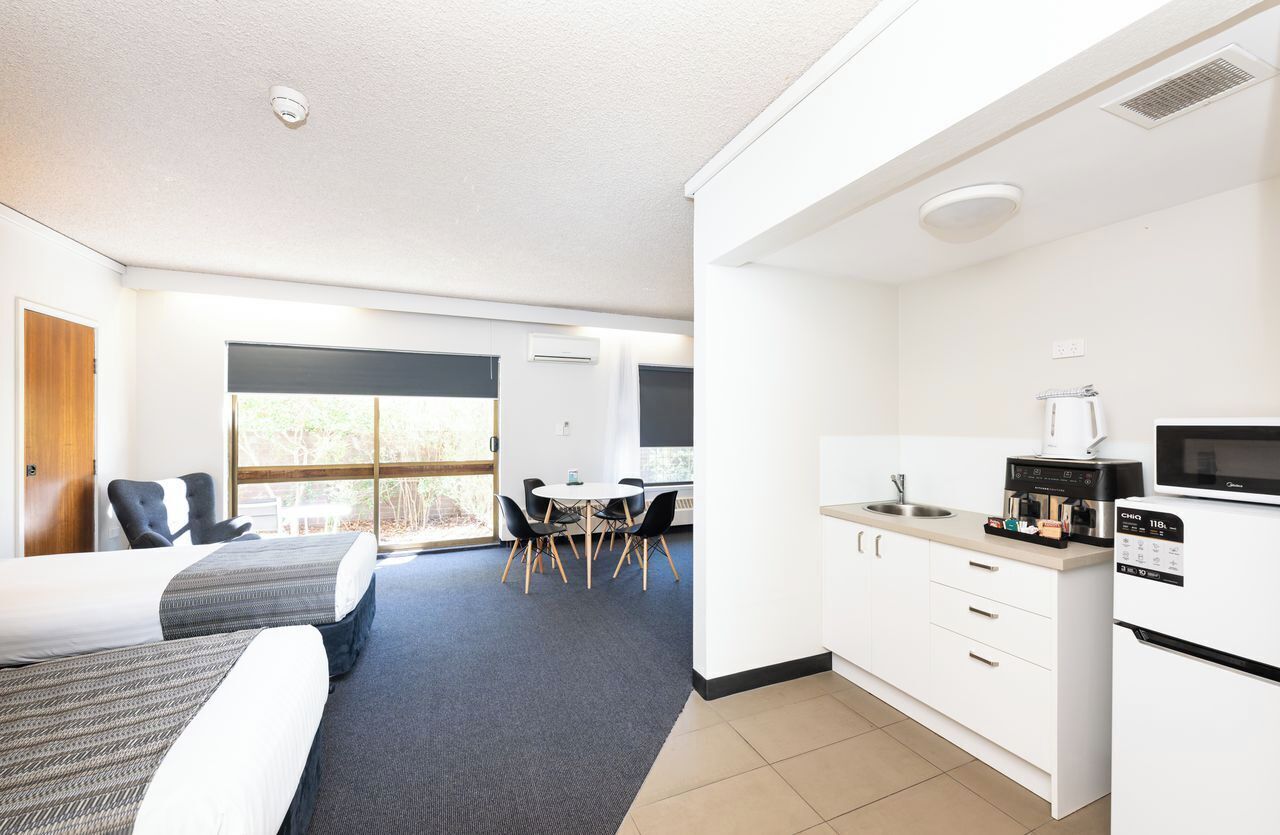 Habitación de hotel moderna con cama, escritorio, silla, kitchenette y vistas al exterior.