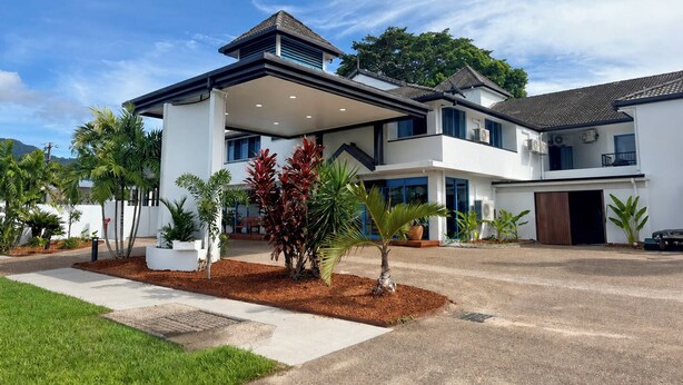 A modern two-story house with a covered patio, a driveway, and landscaped garden with palm trees.