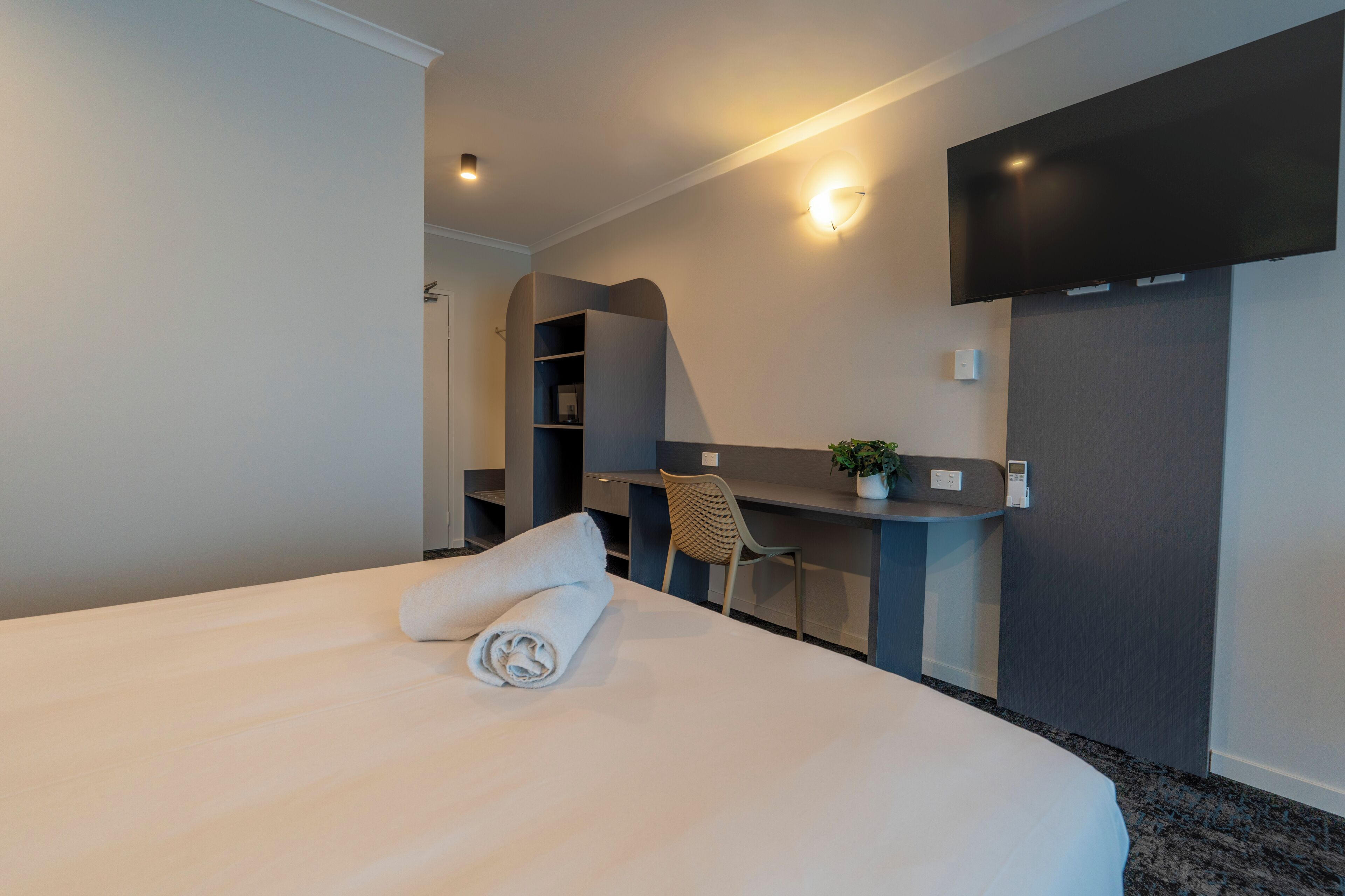 Ein modernes Hotelzimmer mit einem großen Bett, einem Schreibtisch, einem Sessel, einem Flachbildfernseher und einem kleinen Topfpflanzen.