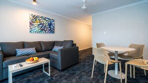 A modern living room with a gray sofa, a coffee table, and a dining area with wicker chairs.