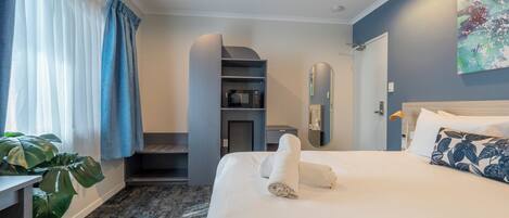 A hotel room with a bed, a desk, a plant, a microwave, and a bathroom door.