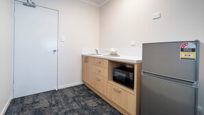A compact kitchen with a white door, wooden cabinets, a stainless steel refrigerator, and a microwave.