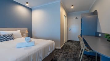A hotel room with a bed, a desk, a chair, a door, and a wall-mounted mirror.