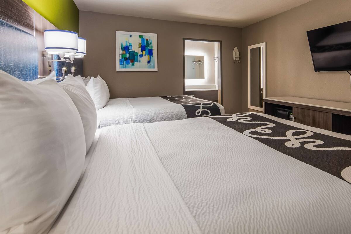 Ein Hotelzimmer mit zwei Betten, einem Fernseher, einem Gemälde und einer Badezimmertür.
