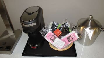A coffee maker, a basket of coffee pods, and a silver teapot on a countertop.