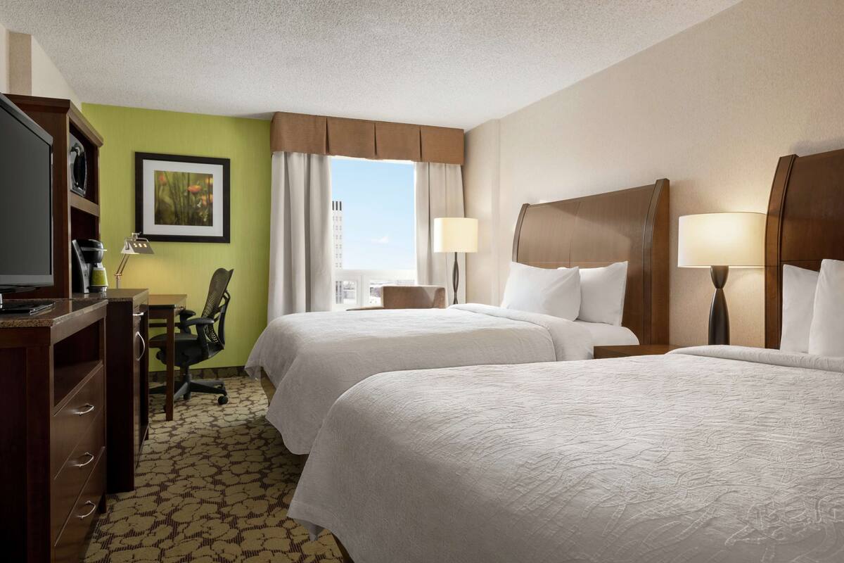 A hotel room with two beds, a desk, a chair, a television, and a window with curtains.