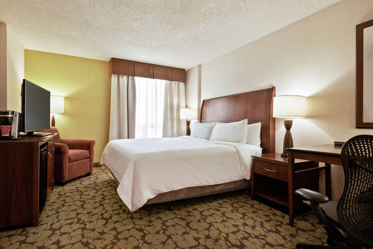 A hotel room with a bed, desk, chair, television, and lamps.