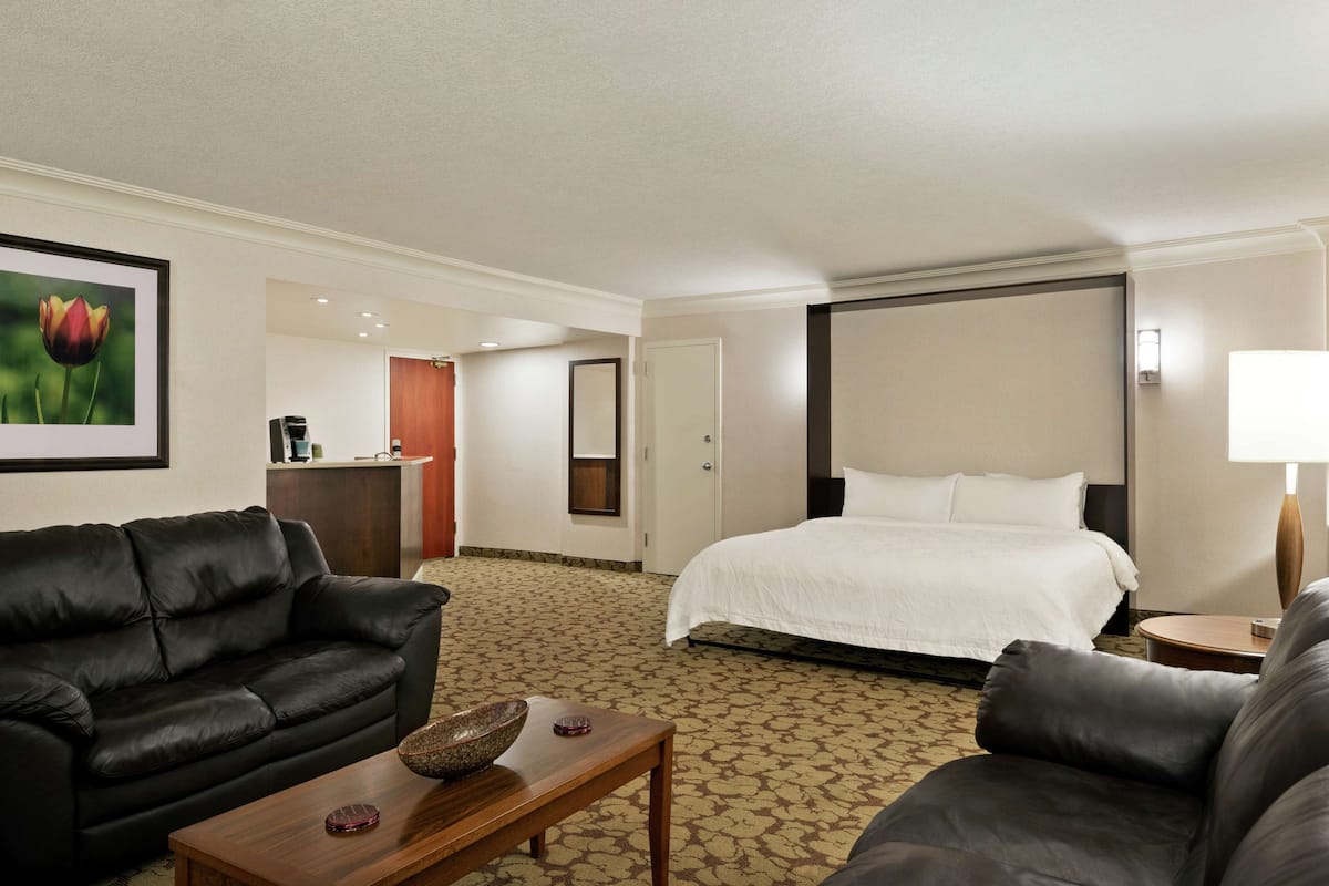 A hotel room with a bed, two sofas, a coffee table, a desk, and a framed picture on the wall.