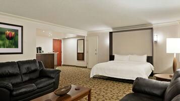 A hotel room with a bed, two sofas, a coffee table, a desk, and a framed picture on the wall.