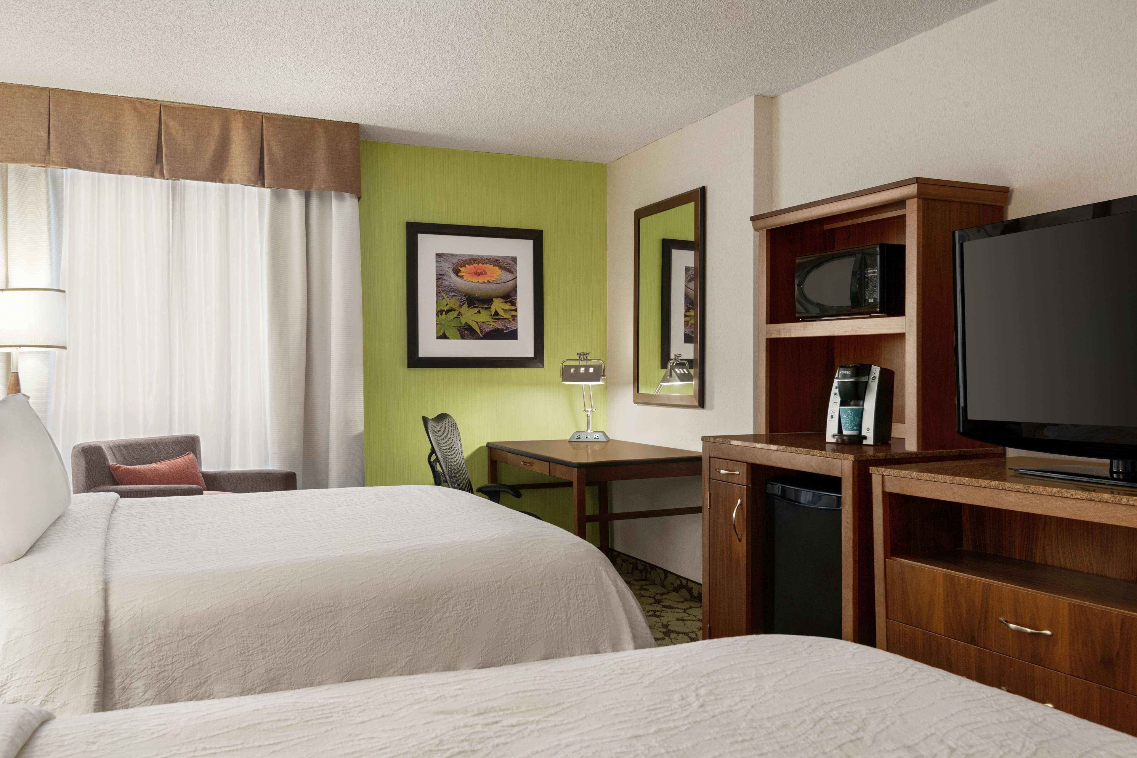 A hotel room with two beds, a desk, a chair, a television, a microwave, and a coffee maker.