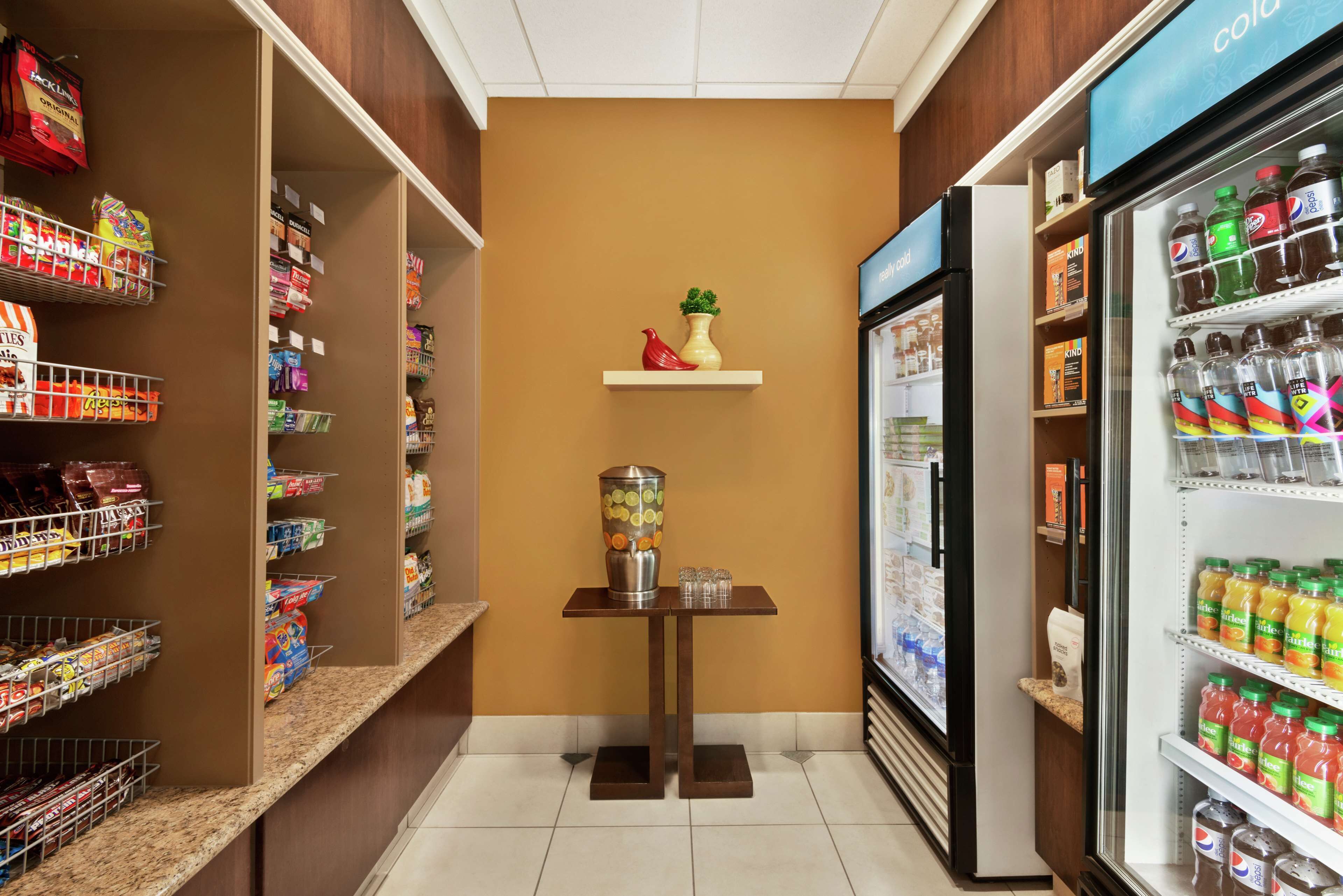 A grocery store interior with shelves stocked with various products, a refrigerated section, and a small table with a vase and salt shakers.