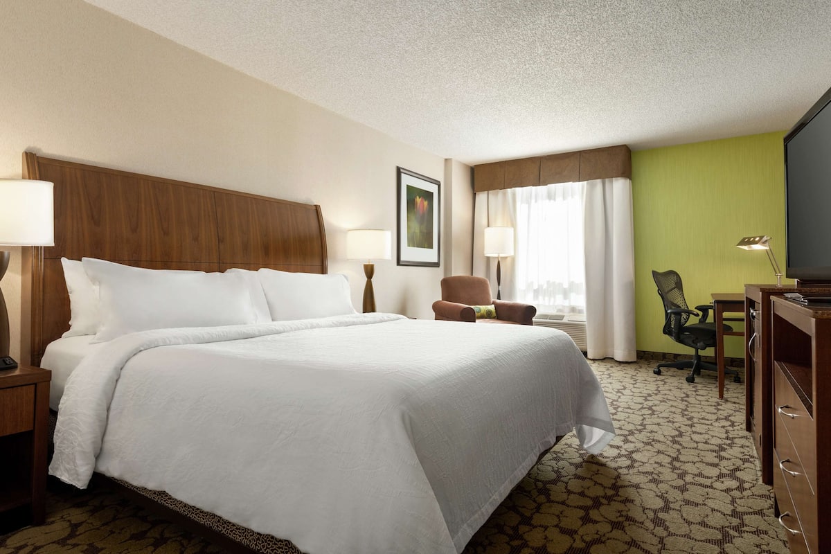 A hotel room with a large bed, two bedside tables with lamps, a desk with a chair, and a television.