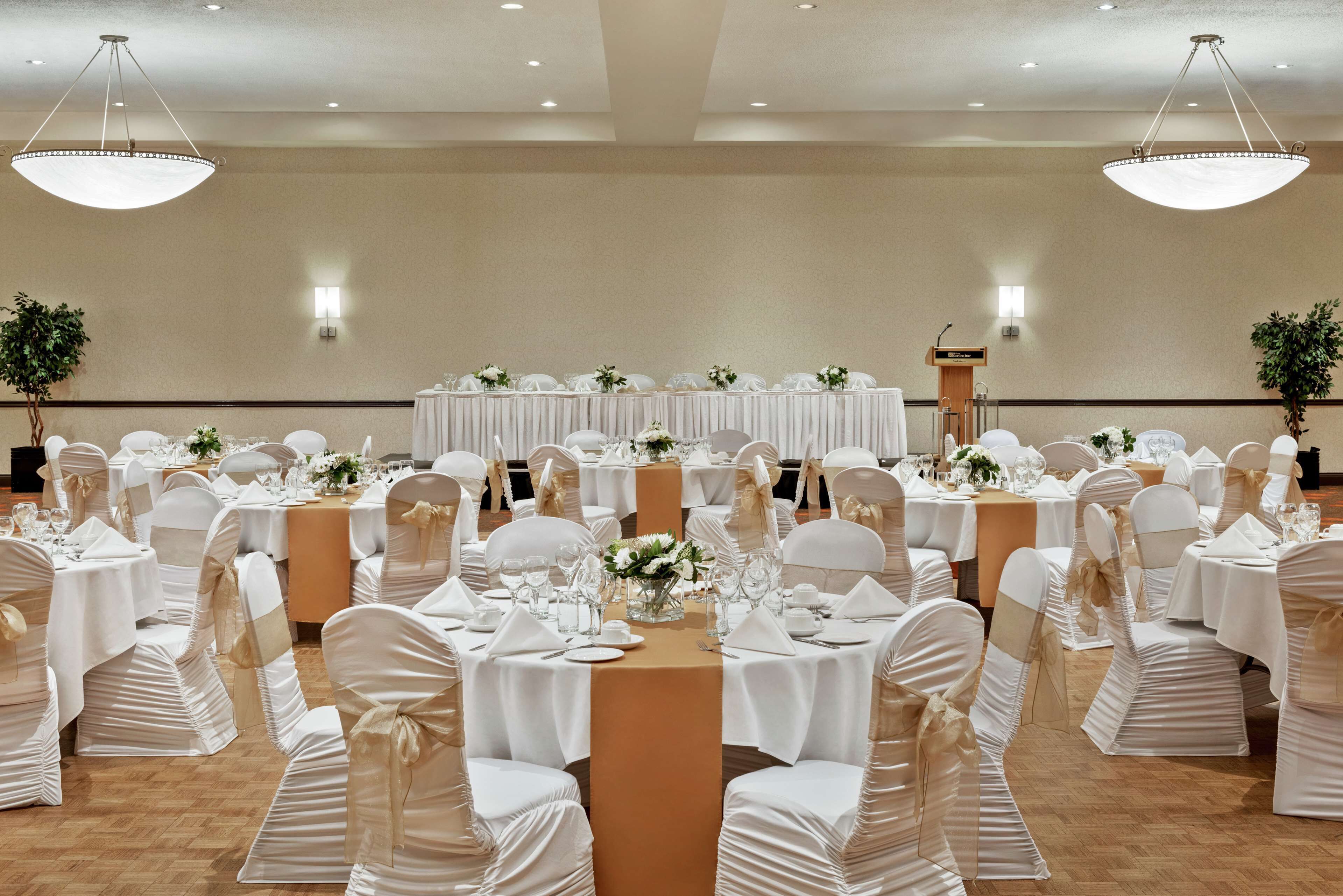 Un salón de banquetes con mesas redondas, manteles blancos y sillas cubiertas de blanco.