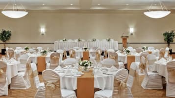 Un salón de banquetes con mesas redondas, manteles blancos y sillas cubiertas de blanco.