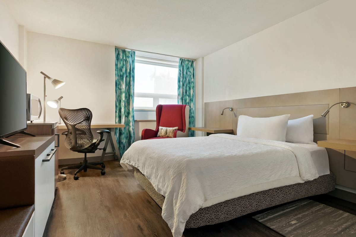 A hotel room with a bed, desk, chair, and a TV.