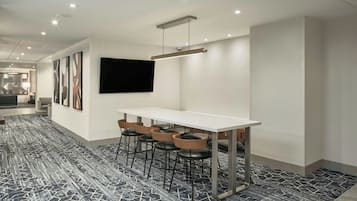 A modern conference room with a white table, four black leather chairs, and a mounted flat-screen TV.