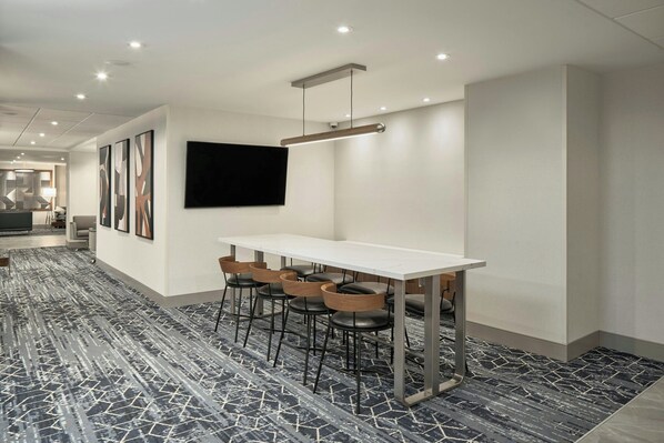 A modern conference room with a white table, four black leather chairs, and a mounted flat-screen TV.