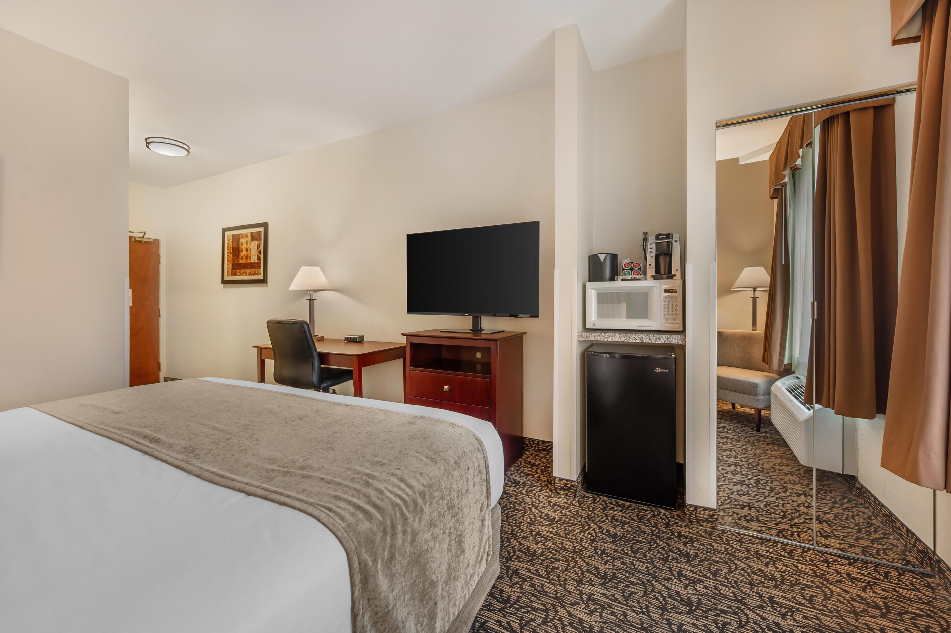A hotel room with a bed, desk, TV, minibar, and a bathroom with a shower curtain.