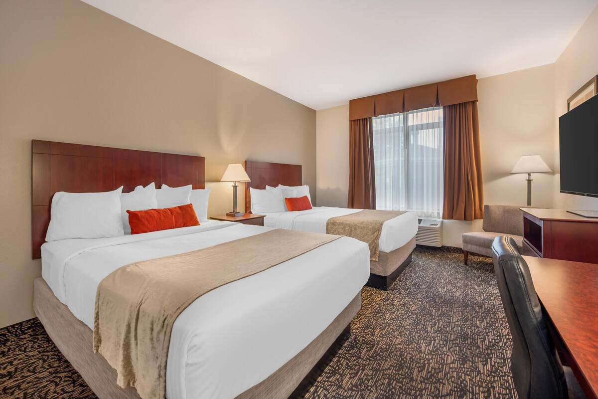 A hotel room with two beds, a desk, a TV, and a window with curtains.