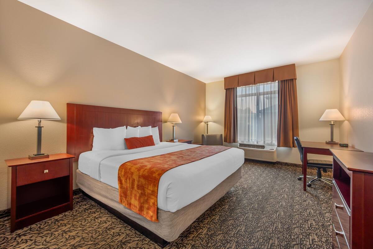 A hotel room with a large bed, two bedside tables with lamps, a desk, and a chair.