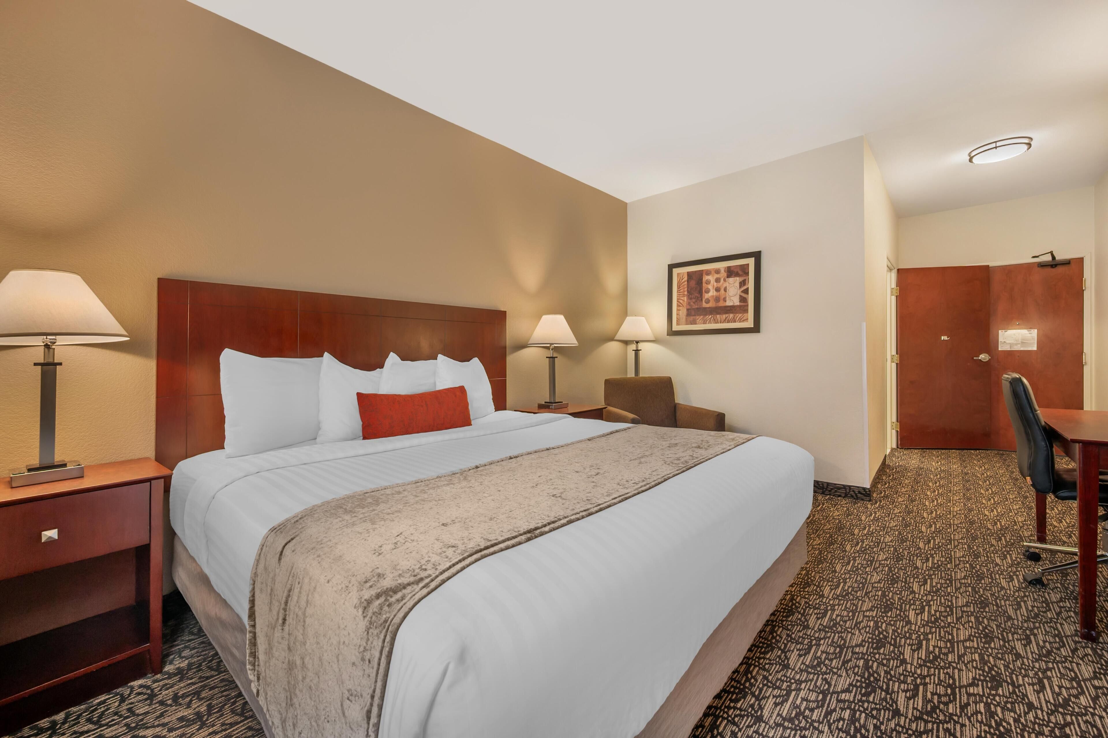 Een hotelkamer met een groot bed, twee bedlampen, een bureau en een stoel.