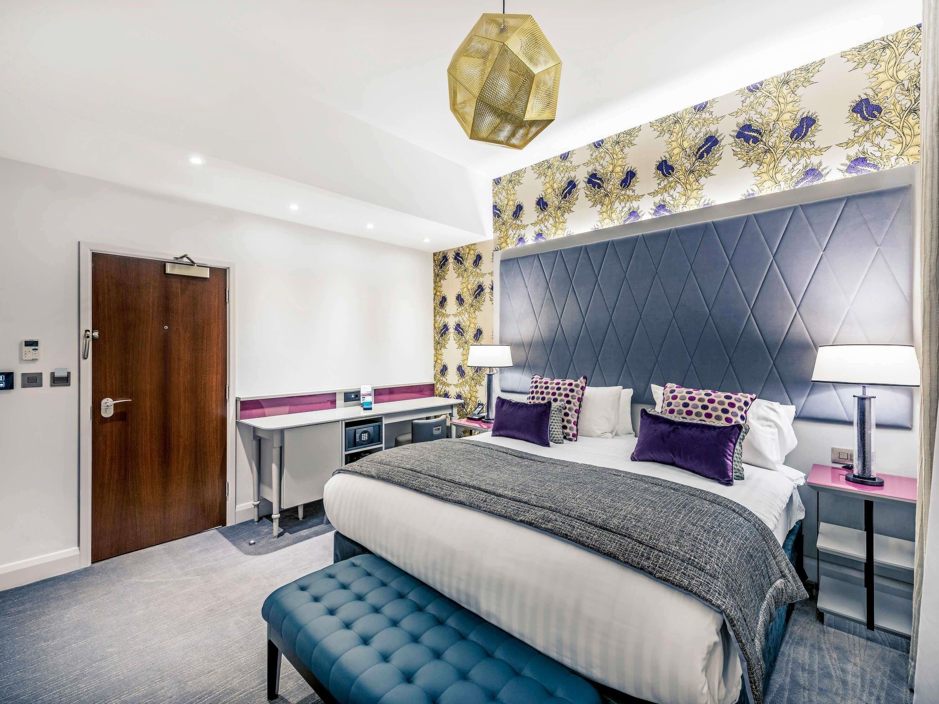 Hotelkamer met een bed, bureau, bankje, hoofdeinde en een behang met patroon.