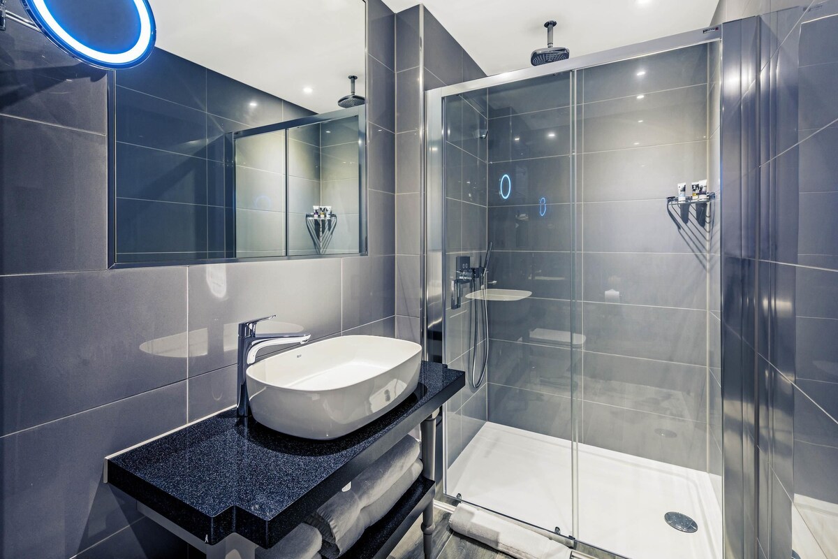 A modern bathroom with a glass-enclosed shower, a large mirror with a blue light, and a granite countertop.