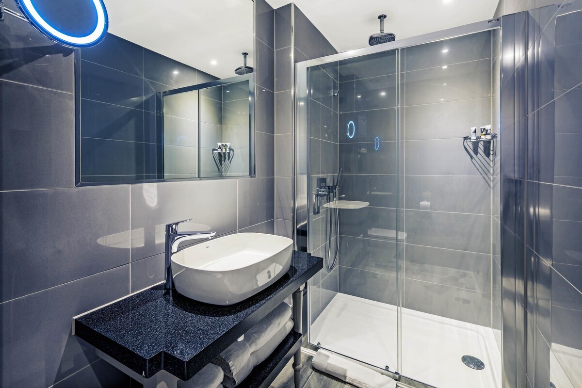 A modern bathroom with a glass-enclosed shower, a large mirror with a blue light, and a granite countertop.