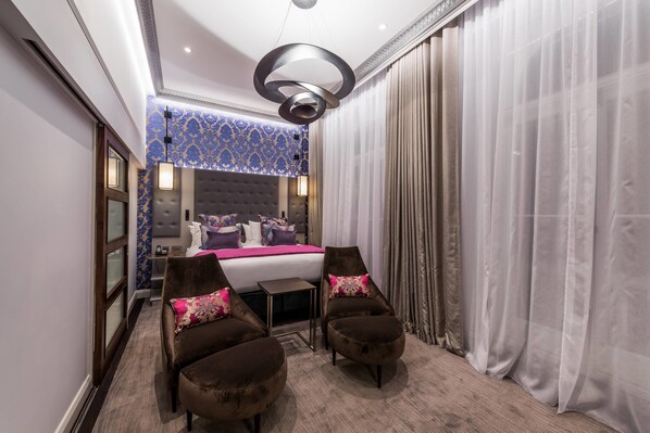 A hotel room with a large bed, two armchairs, a small table, and a decorative ceiling light.