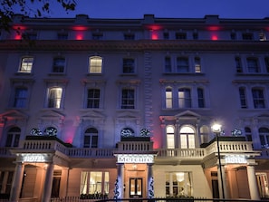 A multi-story hotel with a classical facade, featuring a central entrance with a sign, and balconies with railings.
