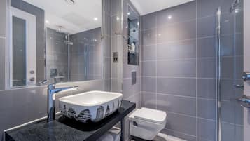 Une salle de bain moderne avec un grand miroir, un lavabo blanc orné d’un motif décoratif, des toilettes et une douche à parois de verre.