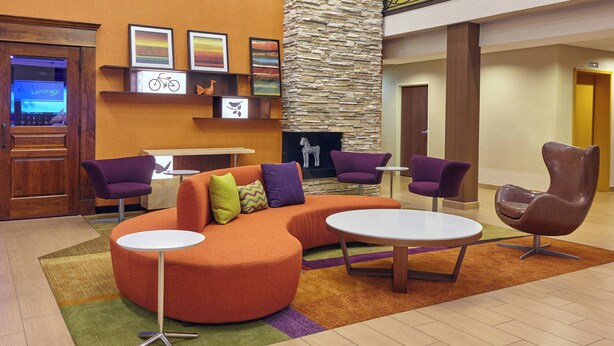 Eine Lobby mit einem gebogenen orangefarbenen Sofa, violetten Sesseln, einem weißen Couchtisch und einer Wand mit Steinverkleidung.