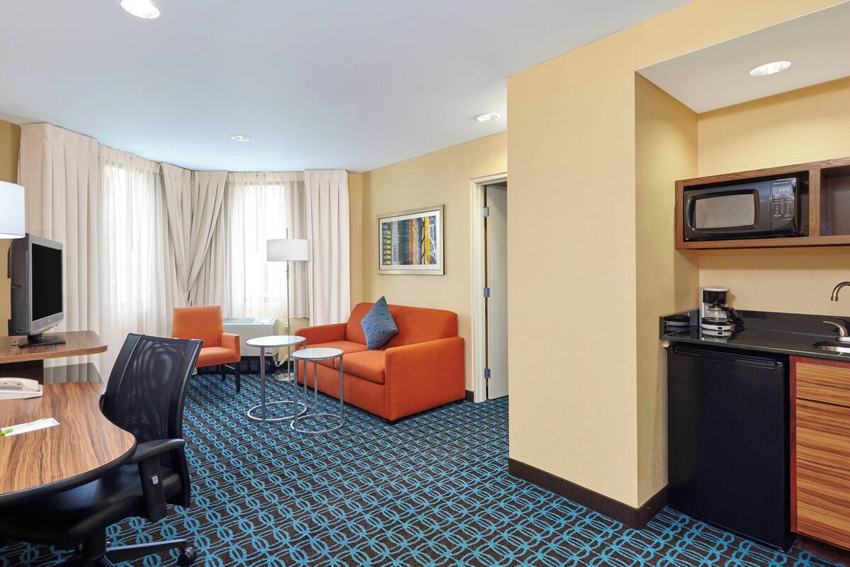 A hotel room with a kitchenette, a dining area with a table and chairs, a sofa, and a television.