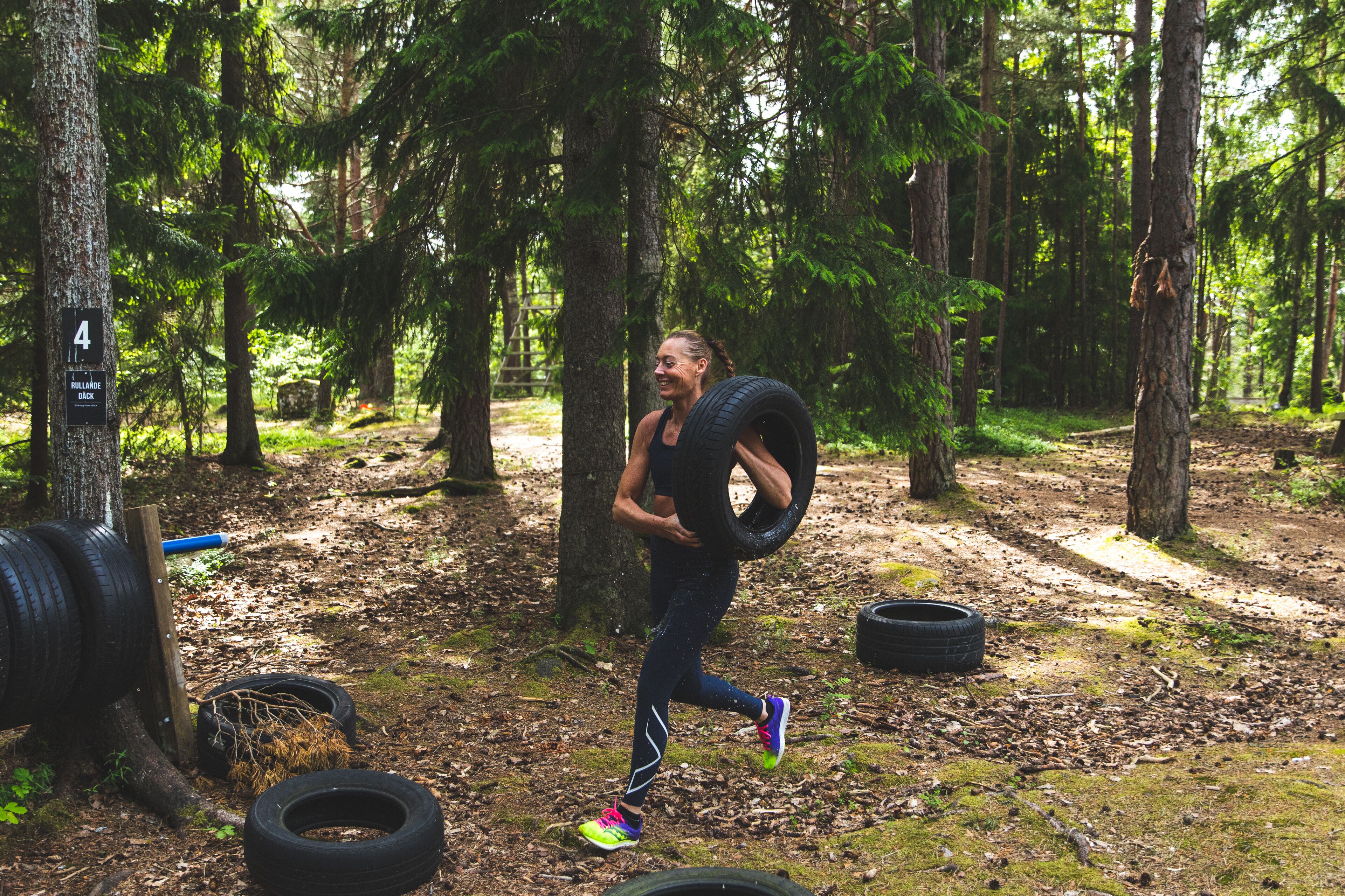 A person running through a forest with trees and scattered tires on the ground.