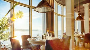 Un comedor con una mesa dispuesta para dos personas, ventanas amplias y vista al agua.
