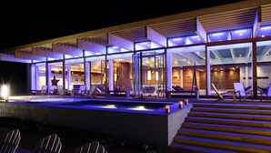 Un edificio moderno con fachada de vidrio, zona de estar exterior con sillas y una piscina.