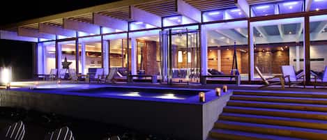 A modern building with a glass facade, outdoor seating area with chairs, and a pool.